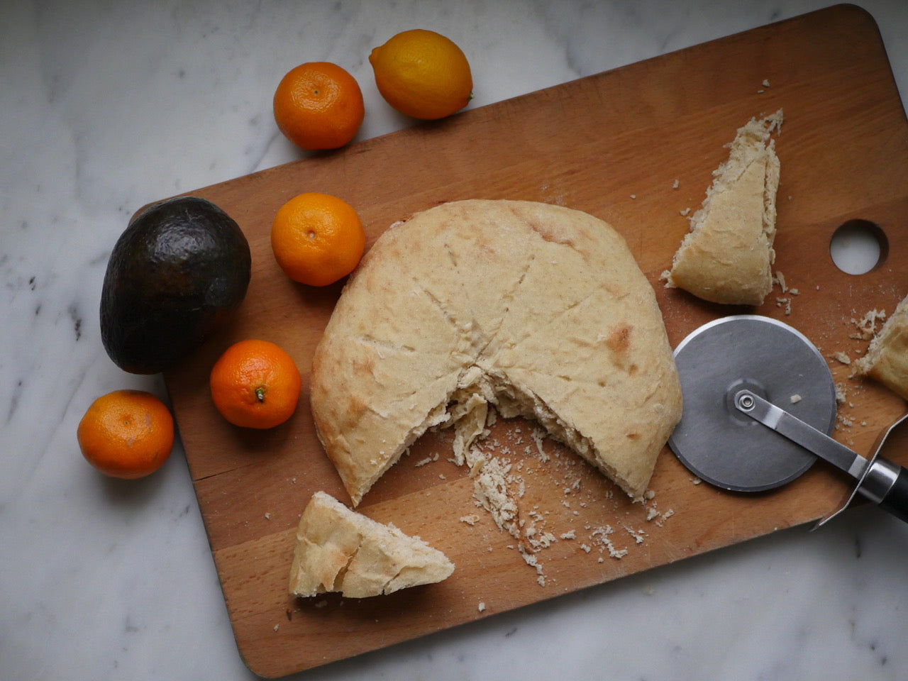 Homemade bread, an avocado, and some mandarins on a cutting board.