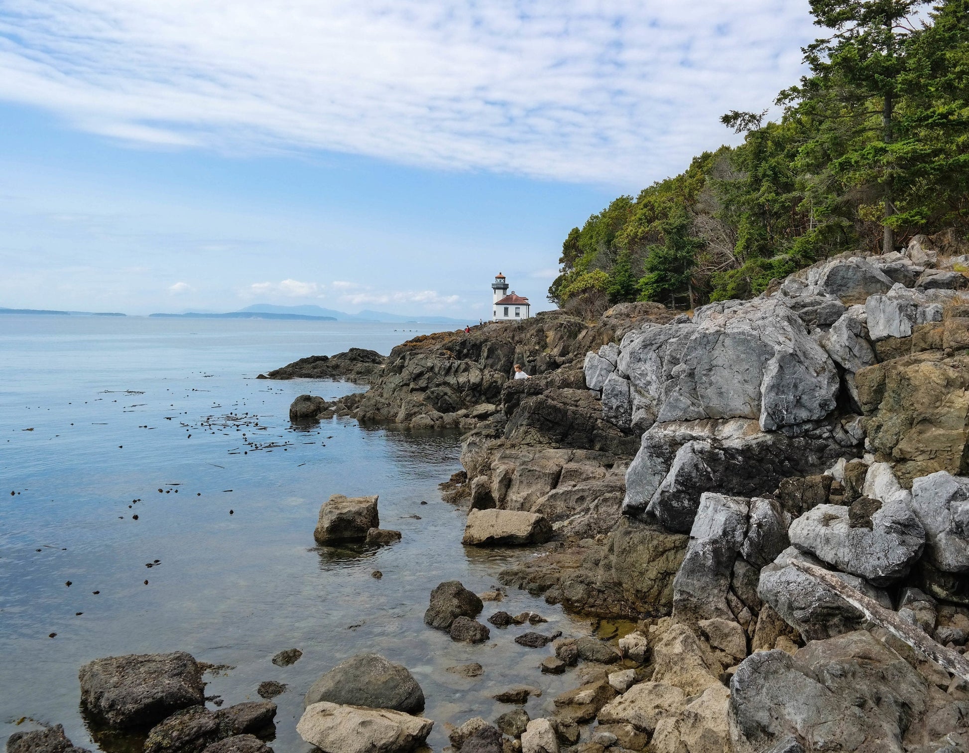 A lighthouse on a rocking coast with a homeschool child looking over the water.