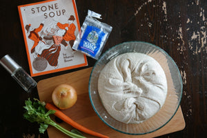 The book "Stone Soup" on a well worn wooden table next to a bowl of sour dough dough made by a homeschool family.